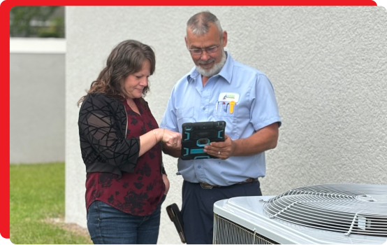 an hvac technician showing a client something on a tablet standing next to an hvac unit outside