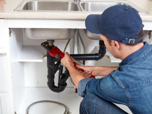 Plumber repairing under-sink pipes while providing residential plumbing service for homeowners